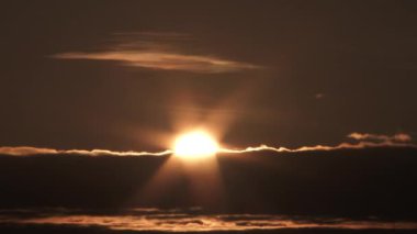 Time lapse of sun rising and revealing behind cloud layer with sky becoming bright as glowing light rises.