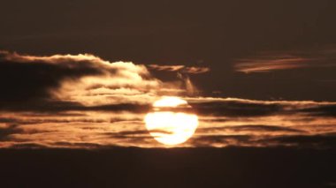 Timelapse of warm lit sky turning black as sun sets behind clouds.