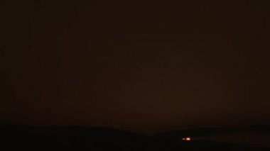 From black, sun rises behind silhouetted landscape and thin cloud layer up into a warm empty sky.