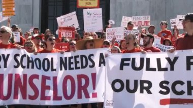 Large group of teachers stand out front of the State Capitol Building chanting 