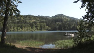 People enjoy the outdoors on summer day fishing from boats at forest lake in the Pacific Northwest.