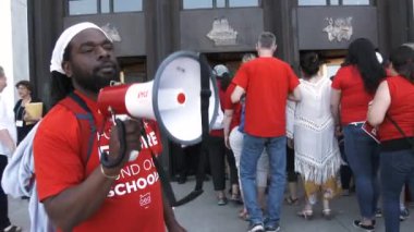 Man with megaphone gets the crowd chanting for more school funding outside government building.