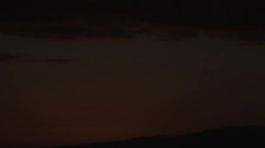 Sunrise timelapse above hillside landscape shining warm and bright on partly cloudy sky.