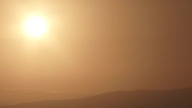 Day to night timelapse, sun setting on warm lit sky falling behind cloud layer and silhouetted landscape.