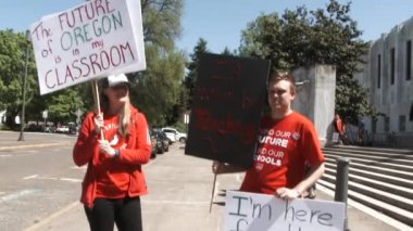 Two teachers stand outside the capitol building holding signs concerned for their schools and lack of funding.