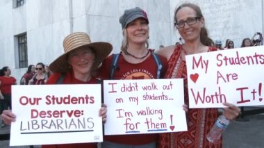 Three teachers stand together with signs letting Congress know schools need more resources.