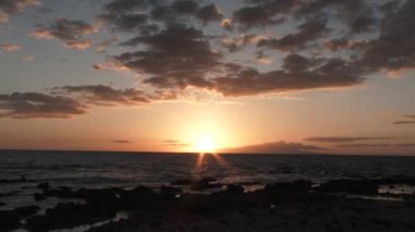 Real time beach scenic at the Pacific Ocean during beautiful sunset with colorful sky as sun sets behind horizon.