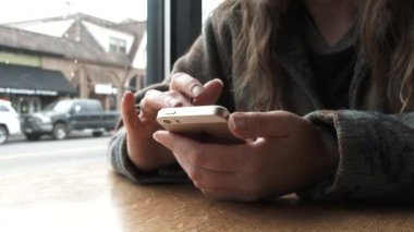 Kahvede oturan bir kadın siparişini beklerken telefonuyla oynaşıyor..