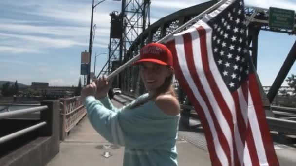 誇り高い女性はアメリカ国旗を振り 身に着けていますアメリカを偉大に再び帽子はドナルド トランプの集会のためにダウンタウンを訪れます — ストック動画