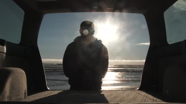 俄勒冈州阳光明媚的一天 坐在汽车尾门上的人影 看着海浪在海滩上破浪而出 然后站起来走出车架 供商业用途的型号 — 图库视频影像