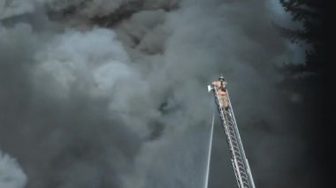 İtfaiyeci, merdivenin sonundan su fışkırtırken alttaki büyük yangından çıkan dumanla yüzleşiyor..