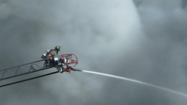 在消防车的梯子上 一名消防员将消防水管对准火源 这时巨大的烟柱经过火源 超过了努力工作的工人 — 图库视频影像
