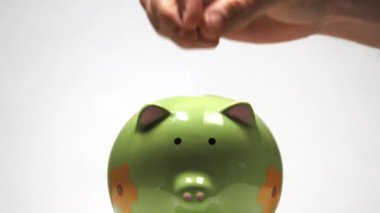 Stüdyoda, birinin eli kumbaraya bozuk para ekler ve üstüne bir dolar daha ekler..
