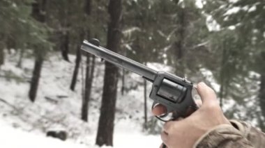 Kışın ormanda, yarı hızda, ağır çekimde yakalanmış bir adam tabancasına nişan alır ve tetiği çeker..