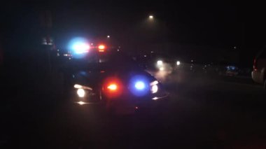 Polis arabası yol kenarına parlayan ışıklarla park etmiş. Gece yol üzerinde bir suç mahalli oluşturuyor..
