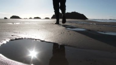 Güneşli bir günde Pasifik Sahili 'nde yürüyen biriyle kumlu sahildeki gelgit havuzuna yansıyan güneş..