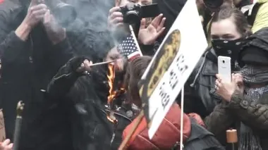 Protestocular, anonim olarak da dahil olmak üzere Portland, Oregon şehir merkezinde toplandılar ve Donald Trump 'ın başkanlığı ele geçirmesine karşı ilk yasa değişikliğini göstermek için Amerikan bayraklarını yaktılar..