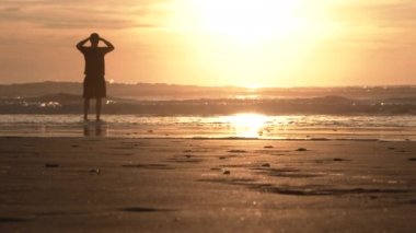 Suyun kenarında duran kişi gün batımında denize bakar..