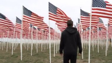 Zencilikten çıkıp, ölen askerlerin anısına rüzgarda dalgalanan Amerika Birleşik Devletleri bayraklarından aşağı inen bir adam..