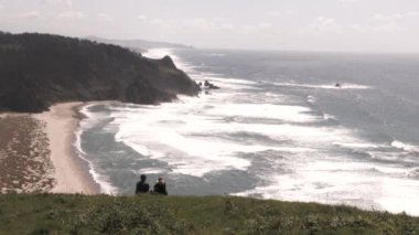 Tanınmayan erkek ve kadın çift, Oregon Pasifik Tepesi 'nin yukarısındaki Pasifik Okyanusu' na bakan çimenli yamaçta oturuyorlar..