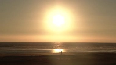 Oregon Sahili 'nde gün batımında insanlar el ele tutuşup sahilde yürüyorlar..