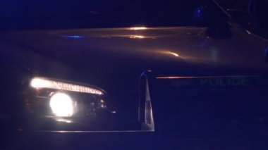 Polis arabasının ön tarafı olay yerinde yanıp sönen ışıklarla çevrili..