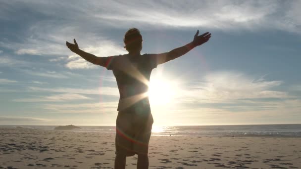 模特儿在俄勒冈州海岸的沙滩上放生了一个男人 看着阳光灿烂的太平洋 在美丽的一天 他把胳膊高举在空中 — 图库视频影像