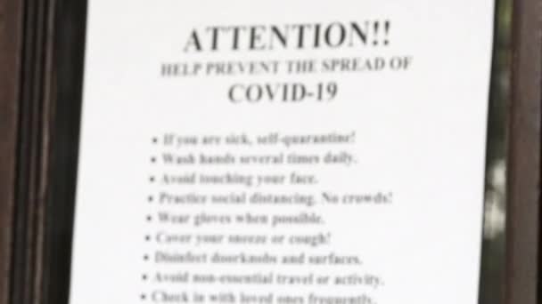 Rack focus on sign posted on door bringing to attention to help prevent the spread of COVID-19.