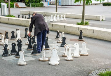 Lozan İsviçre 'de güzel takım elbiseli yaşlı bir vatandaş dev satranç taşlarıyla meydanda açık havada satranç oynuyor.