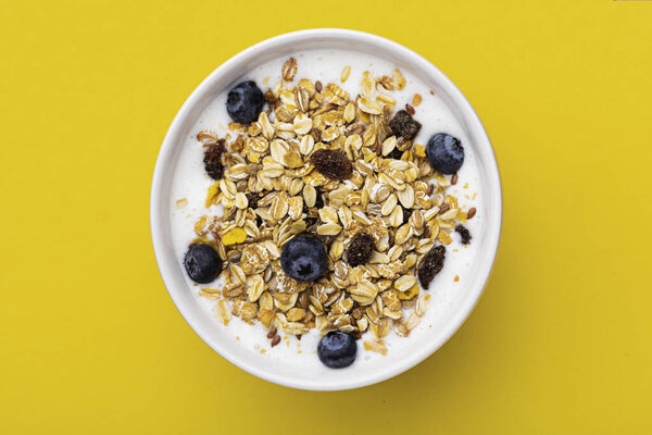 Muesli with yoghurt in a bowl on yellow background