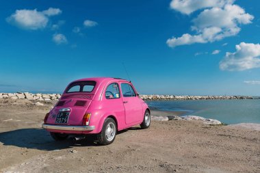 Pedaso, İtalya - 20 Şubat 2016: Bulutlu mavi gökyüzü ile denize yakın eski pembe Fiat Nuova 500 şehir araba park edilmiş. 1957 ve 1975 arasında İtalyan üretici Fiat tarafından üretilen.