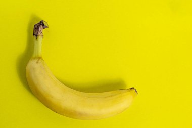 Fotokopi alanı olan sarı bir zemin üzerinde muz. Tasarım, proje, kartpostal için resim. Sarı kağıt üzerinde olgun meyve.