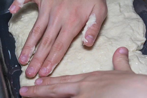 Children's hands spread the pizza dough on a baking sheet. Cooking pizza at home. A popular Italian dish worldwide. — Stock Photo, Image