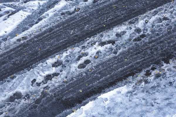 Следы на мокрой дороге, покрытой первым снегом. Начало зимы, первый снег, таяние первого снега . — стоковое фото