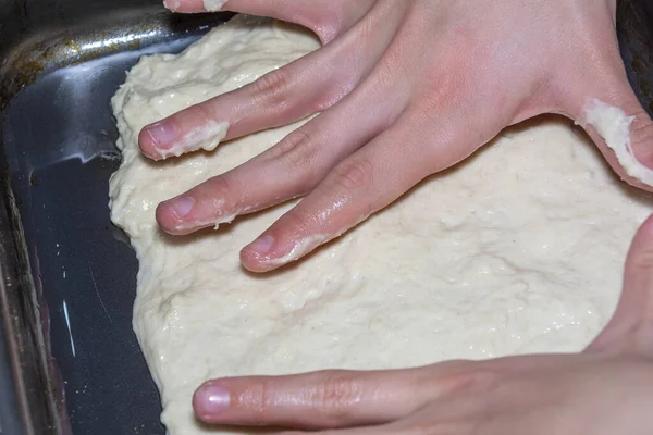 Las manos de los niños extienden la masa de pizza sobre una bandeja para hornear. Cocinar pizza en casa . — Foto de Stock