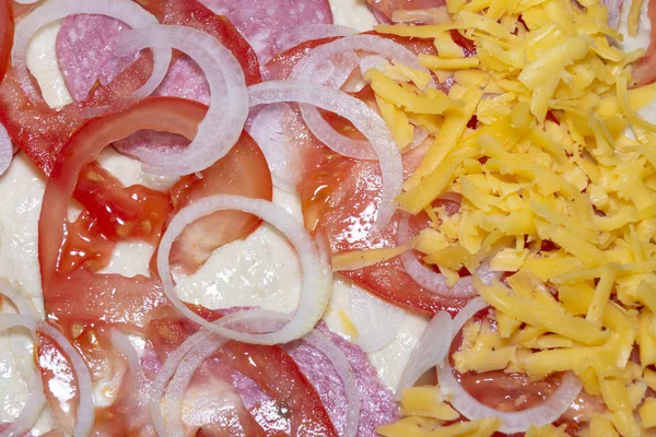 Background of a piece of pizza with ham, tomatoes, onion and cheese. A fragment of pizza in the cooking process close-up. View from above. background — Stock Photo, Image