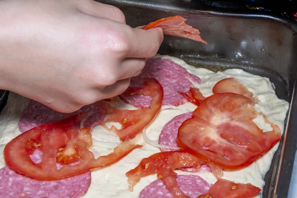 Pizzát főzök. A kéz paradicsomszeleteket rak a tésztára. Közelkép. — Stock Fotó