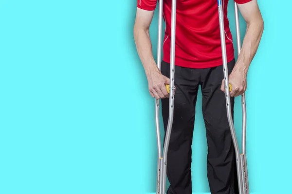 man on crutches isolated on a blue background. Concept: leg injuries, restrictions on human movement, limited abilities.