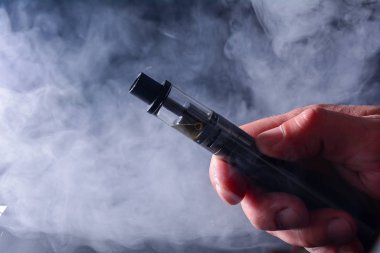 Arka plandaki dumanlı bir elde elektronik sigara görüntüsü. Sigara içmenin tehlikeleri, geleneksel sigaraya alternatif. Kötü alışkanlıklar. güvenli elektronik sigara.