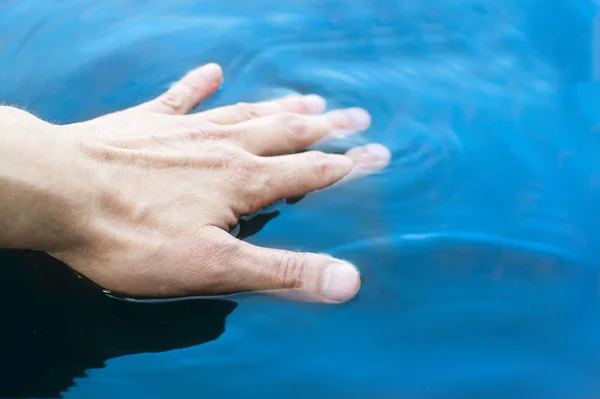Man 's hand touches clean blue water — стоковое фото