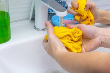 Bir su akıntısının altında kumaş ellerde. Bir kadın ve bir çocuğun elleri. Sarı bez ve eller suyun altında. Konsept: hijyen ve temizlik, eğitim, temizliğin bakımı.