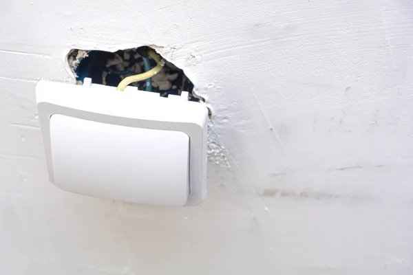 Ηλεκτρικός διακόπτης κατά την εγκατάσταση. Κλείσιμο διακόπτη στο φόντο ενός λευκού τοίχου και ενός κουτιού στερέωσης με καλώδια. — Φωτογραφία Αρχείου