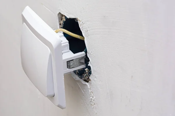 Interruptor eléctrico durante la instalación. Interruptor de cierre en el fondo de una pared blanca y una caja de montaje con cables . — Foto de Stock