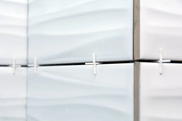 crosses on a white tile. close-up. white tile glued to the wall with white plastic crosses.