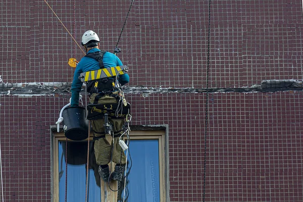 Un escalador industrial trabaja. escalador industrial hace reparación de las paredes de un edificio de varios pisos — Foto de Stock