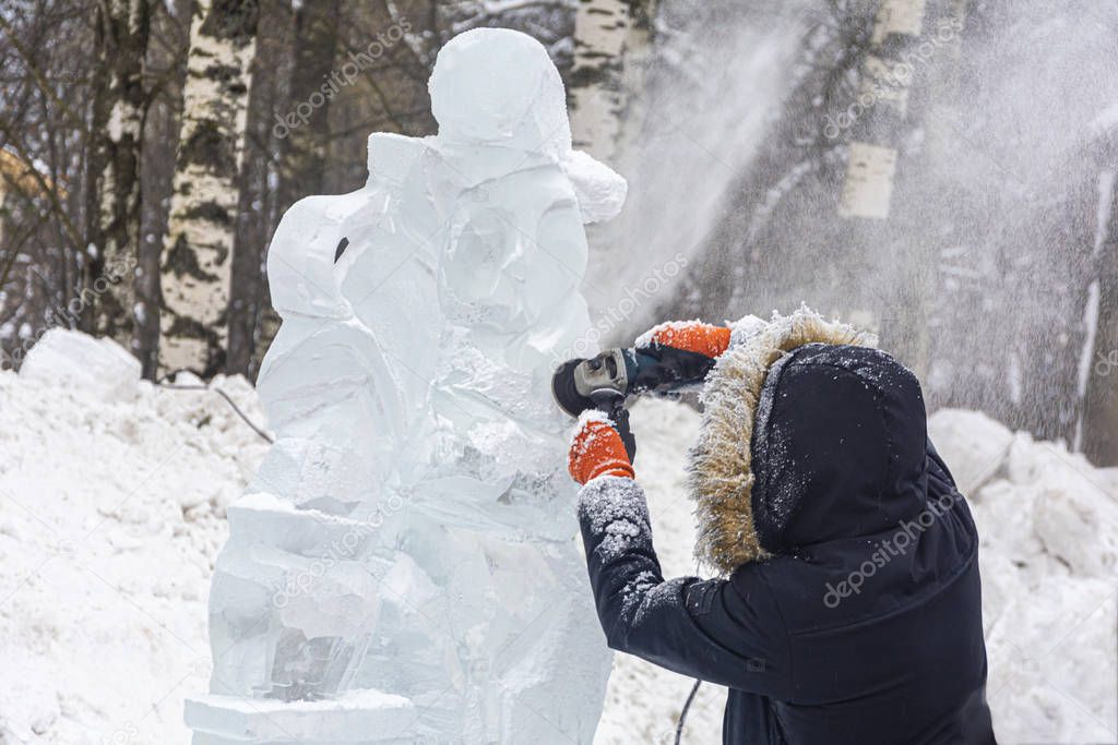A man processes ice. An ice cutter works with tools and polishes ice to make a frozen sculpture at an ice sculpture festival.