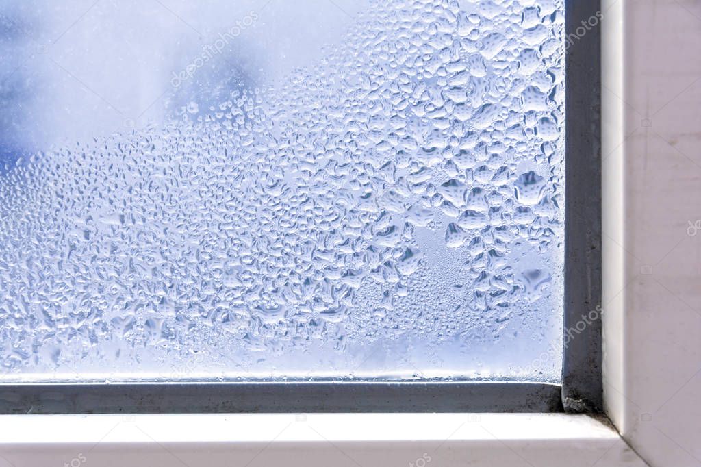 A fragment of a plastic window with condensation of water on the glass. Concept: defective plastic window with condensation, temperature difference, cooling, humidity in the room.