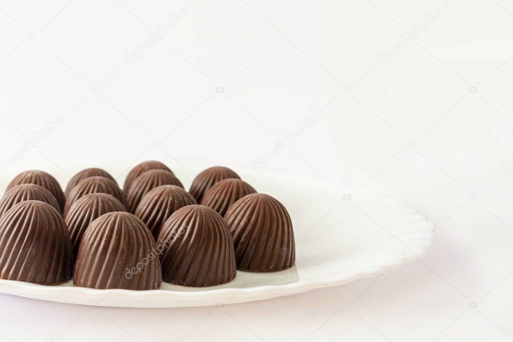Chocolate candies in a white plate. Image on a white background, copy space.