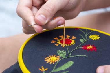 Bir kadın eli bir çemberin içine nakış işliyor, bir kadın karanlık maddeye bir desen işliyor. Yakın plan. Örgü işi, hobi, eğlence konsepti..