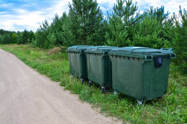 Modern bir Avrupa köyünde yol boyunca yerleştirilmiş yeşil plastik çöp konteynerleri. Ayrı çöp toplama, ekoloji, çevre koruma kavramı.